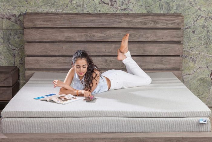 A young woman relaxing on a bed with a magazine and cellphone, set against a stylish wooden headboard.