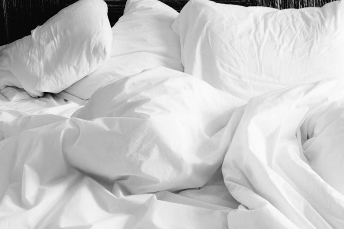 A cozy, rumpled white bed with soft sheets and pillows in a modern bedroom setting.