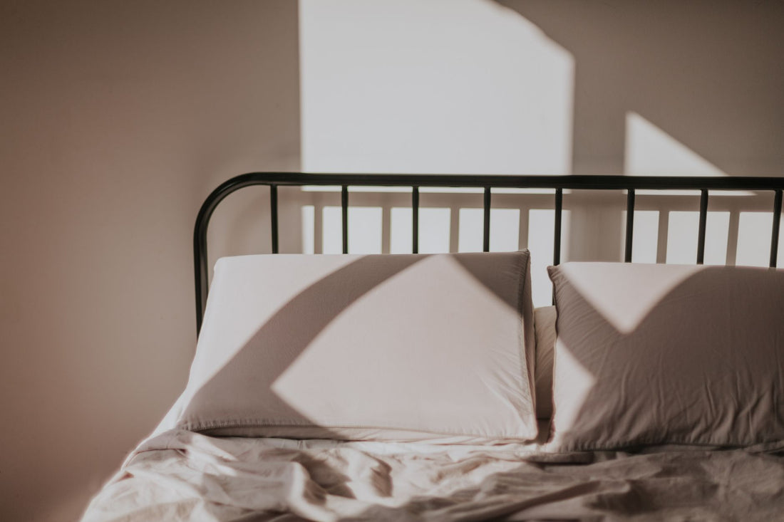 Sunlight casting geometric shadows on a bed with pillows, creating a serene morning atmosphere.