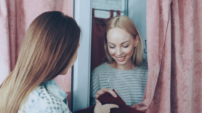 Two women having fun and sharing fashion choices in a fitting room.