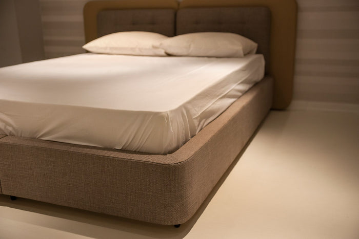 A close-up view of a minimalist bedroom featuring a bed with white linen sheets and plush pillows.