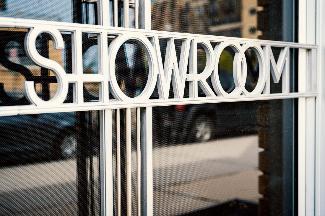Store with Showroom title on glass window reflecting tiled pavement and road with cars behind multistage building in town in daylight