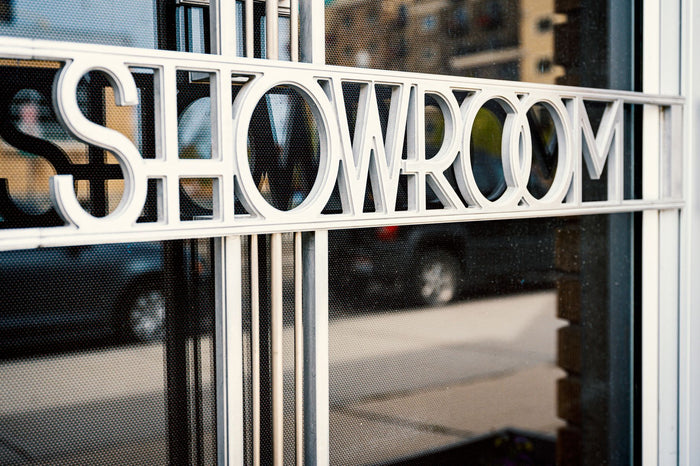 Store with Showroom title on glass window reflecting tiled pavement and road with cars behind multistage building in town in daylight