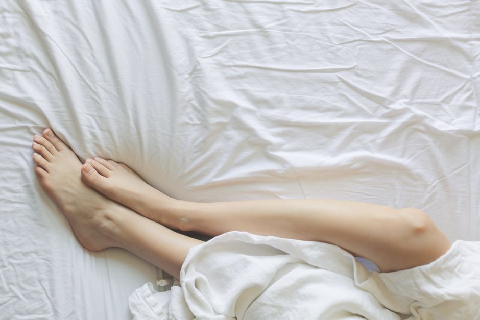 Peaceful morning scene with woman's legs resting in bed under white sheets.
