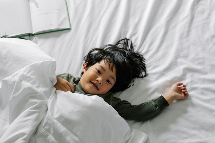 From above of relaxed Asian kid lying in comfortable bed under soft duvet in bedroom