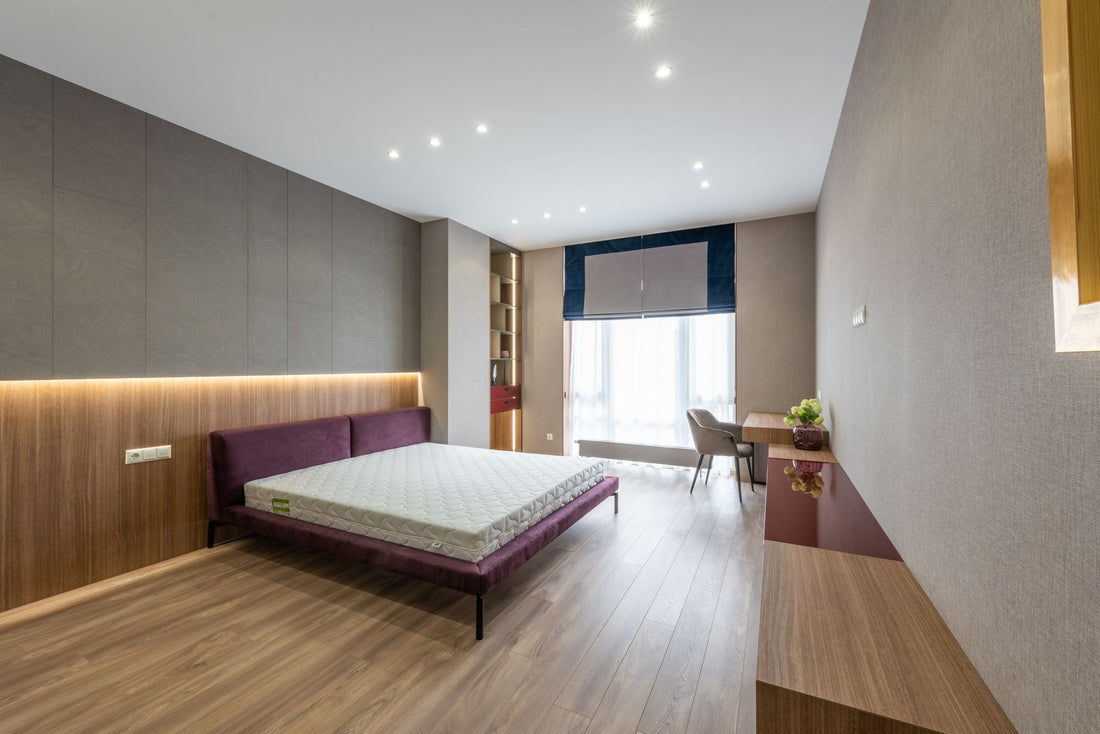 Interior of modern bedroom with white mattress on bed placed at wall near window against wooden cupboards and table with chair