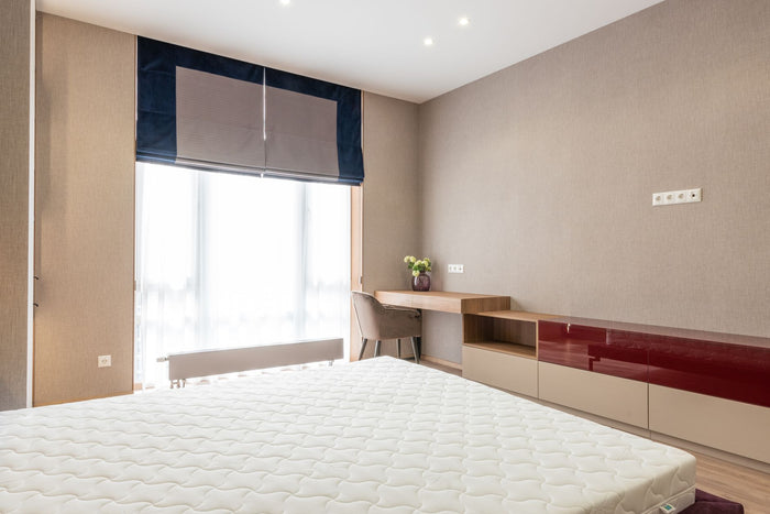 Interior of modern bedroom with mattress on bed placed against wooden cupboard and table with green plant near big window