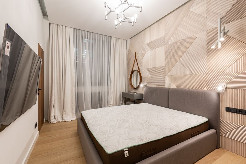Comfortable bed with mattress placed in front of modern TV in cozy bedroom with creative lamps and wooden floor