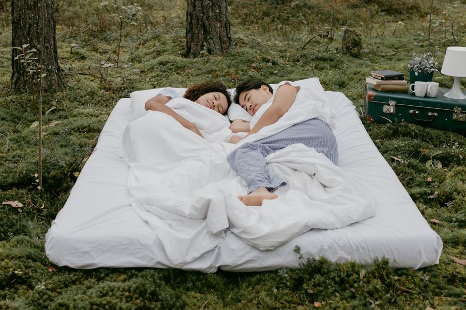 A couple relaxes in the forest, lying on a comfortable mattress surrounded by nature's tranquility.