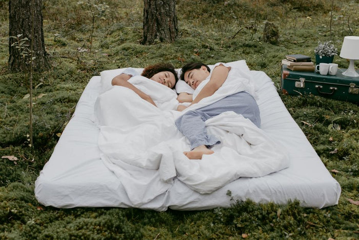 A couple relaxes in the forest, lying on a comfortable mattress surrounded by nature's tranquility.
