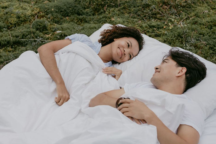 Happy interracial couple lying on a white blanket outdoors, enjoying each other's company and nature.