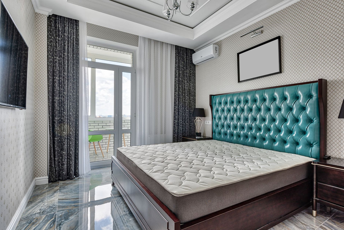 Bed with mattress between bedside tables on tiled floor in apartment with television on ornamental wall