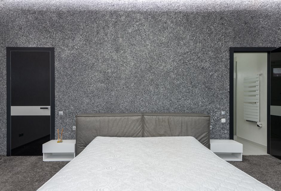 Mattress on bed between tables with statuette in light house with gray carpet and towel rail in bathroom