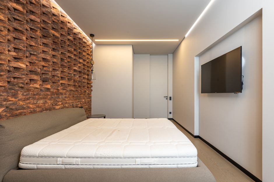 Comfortable be with soft mattress in stylish minimalist bedroom with modern TV and creative brick wall