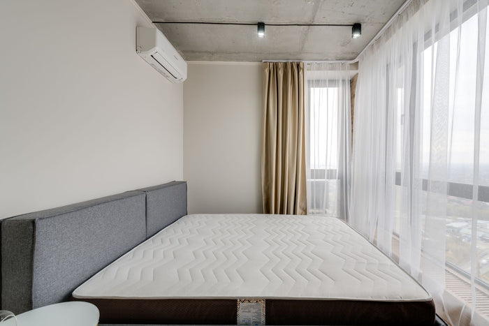 Spacious modern bedroom with a clean mattress and large windows for natural light.