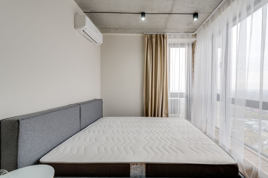 Spacious modern bedroom with a clean mattress and large windows for natural light.