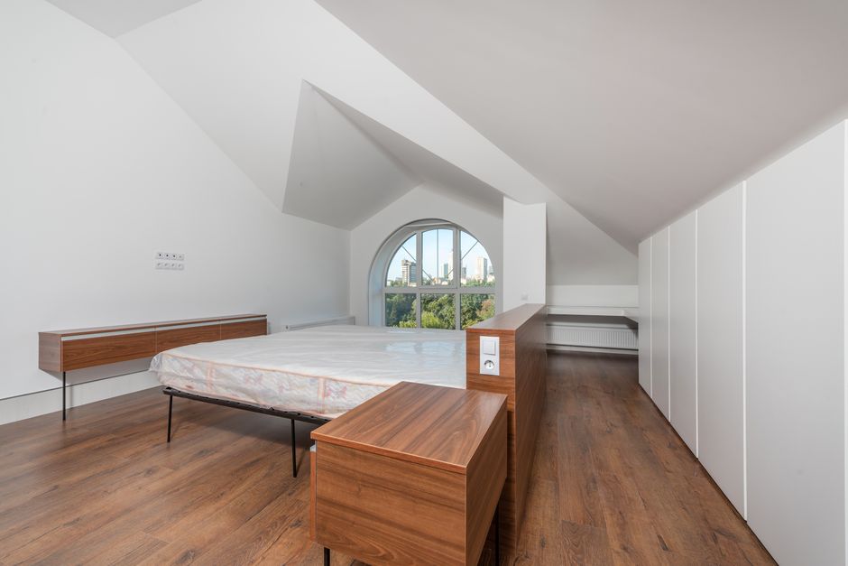 Spacious modern bedroom with minimalist design and wooden flooring, featuring a large window view.