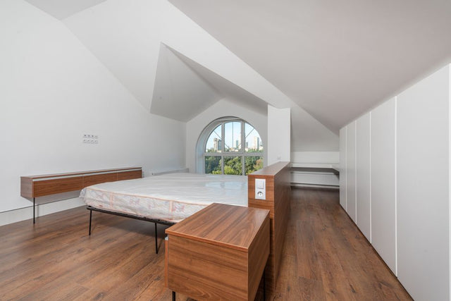 Spacious modern bedroom with minimalist design and wooden flooring, featuring a large window view.