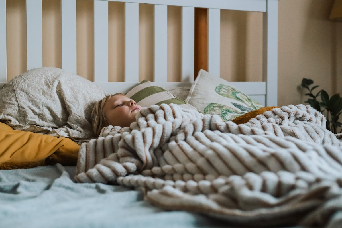 a small child sleeping under a blanket on a bed