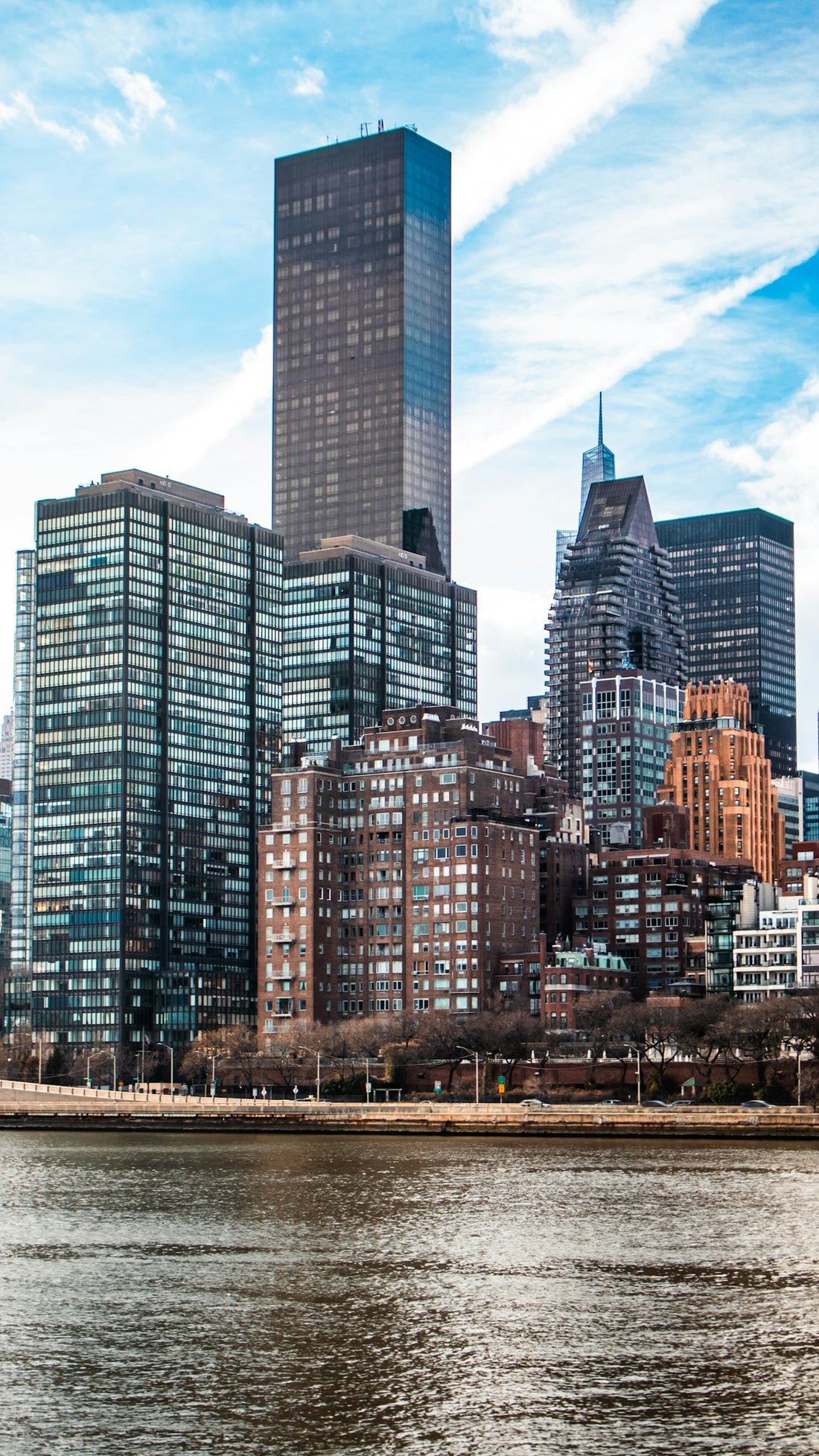 Skyscrapers stand by a river on a beautiful, cloudy day.