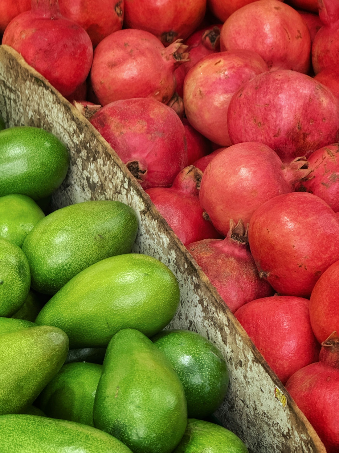 Green avocados and red pomegranates in crates