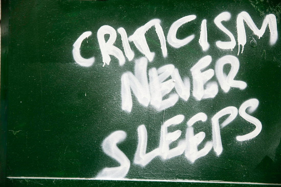 Graffiti on a green wall reads criticism never sleeps