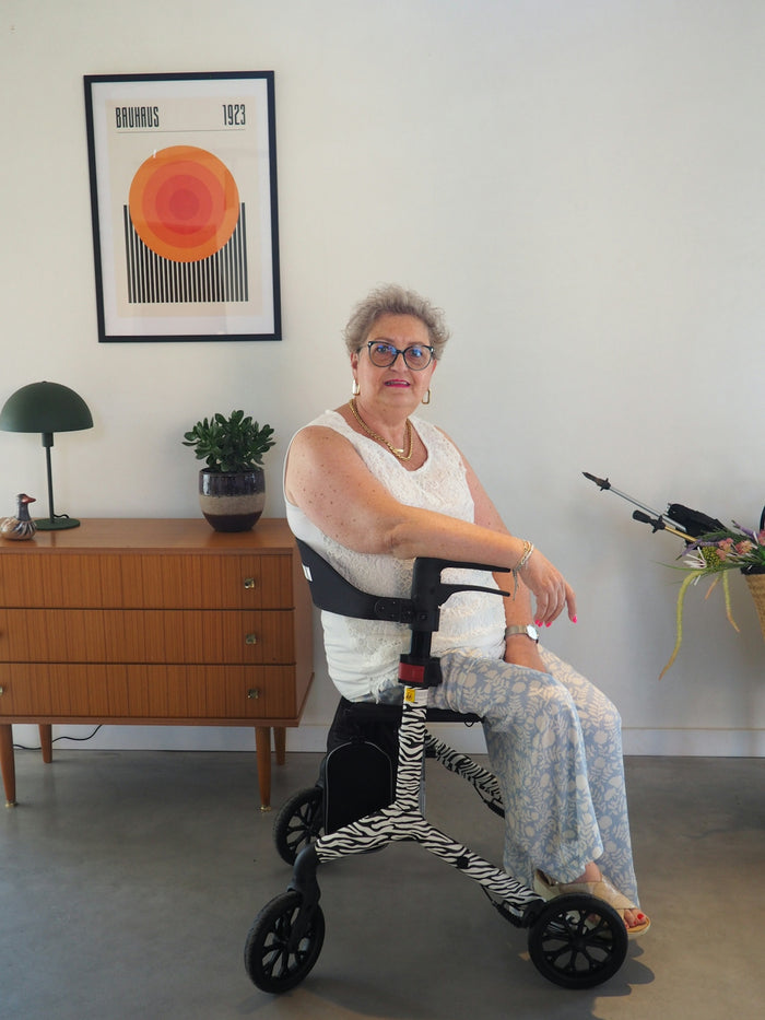 Smiling older woman sitting on a stylish zebra-print walker indoors